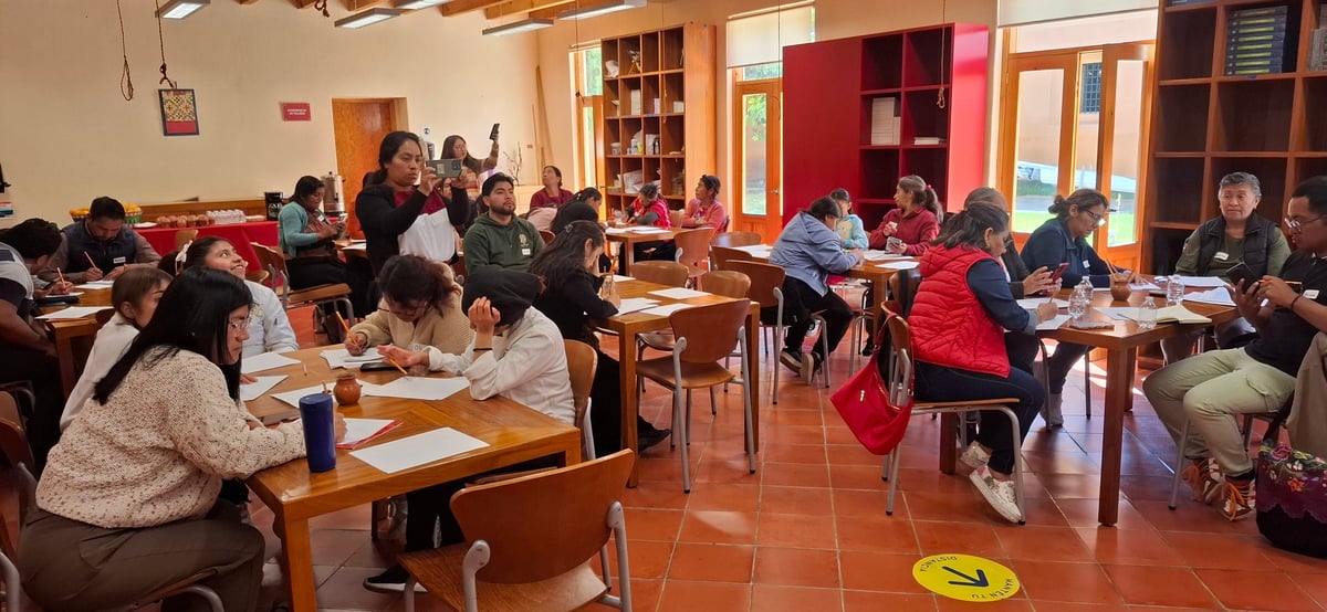 Grupo de estudiantes y docentes trabajando en mesas de madera dentro de un aula colorida.