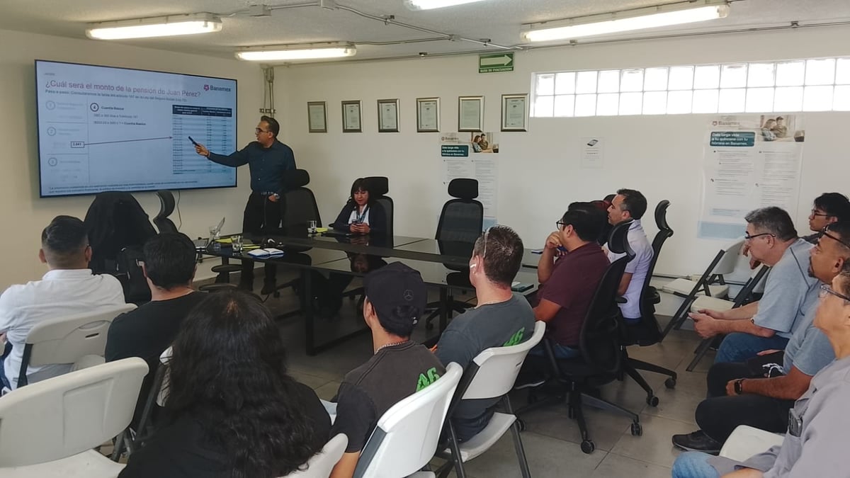 Grupo de personas en una sala de juntas atendiendo una presentación frente a una pantalla.