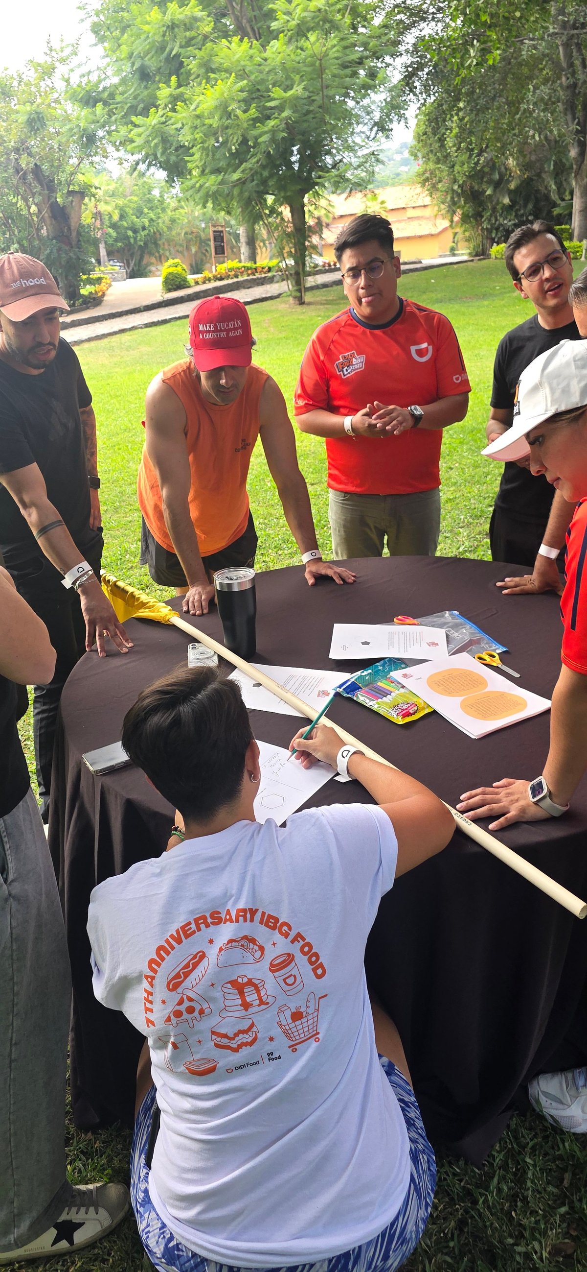Grupo de personas reunidas alrededor de una mesa en un parque durante una actividad al aire libre.
