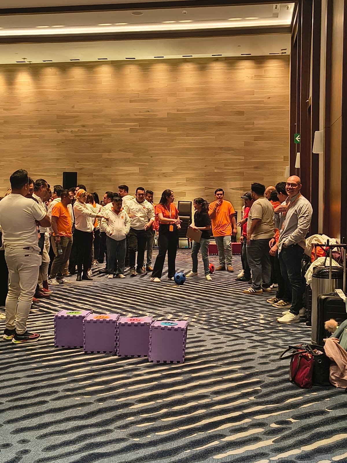 Grupo de personas con camisetas naranja y blanco formando un círculo durante una dinámica de integración en interiores.