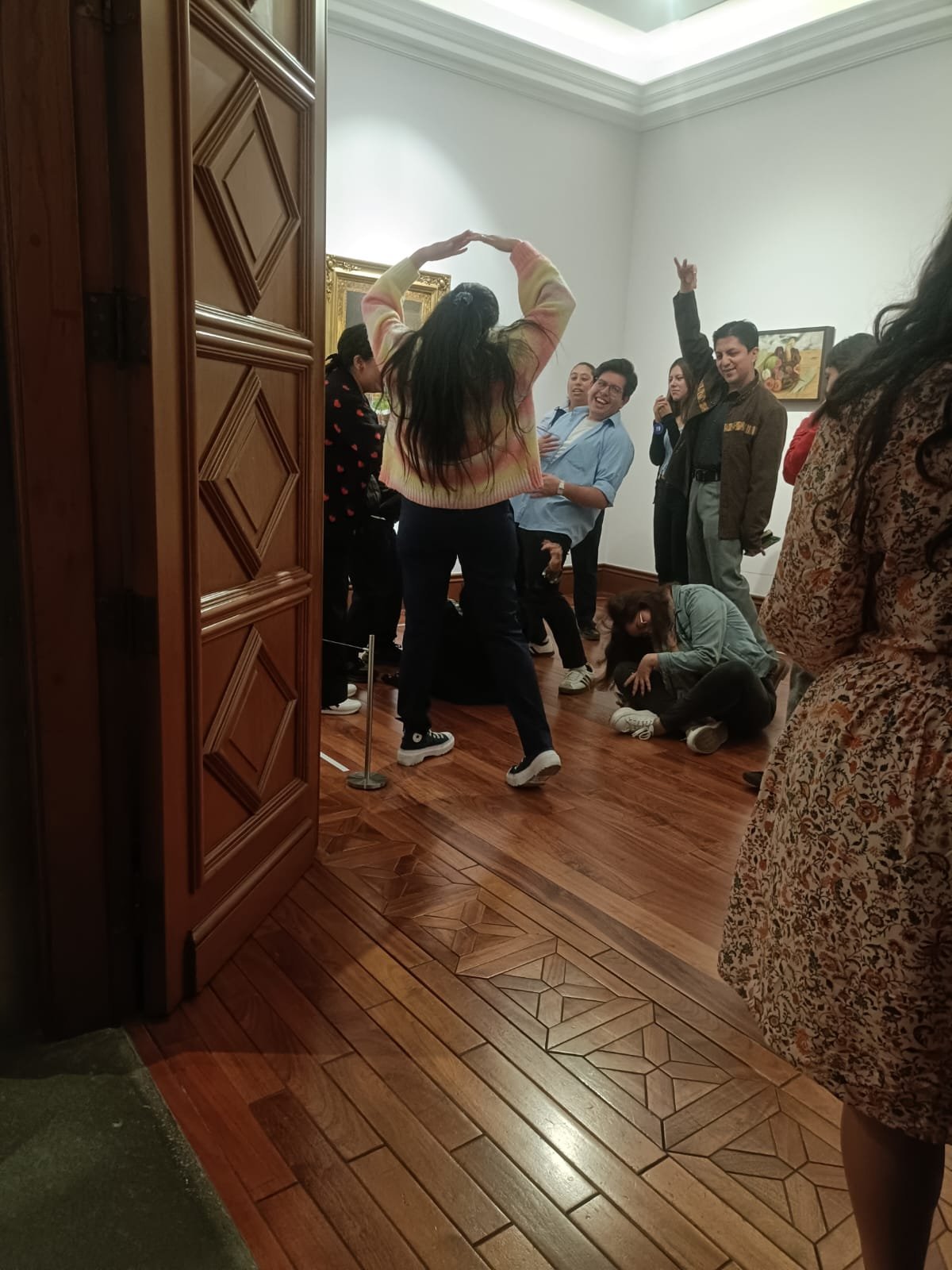 Equipo de jóvenes bailando y celebrando en una sala con piso de madera, con los brazos en alto.